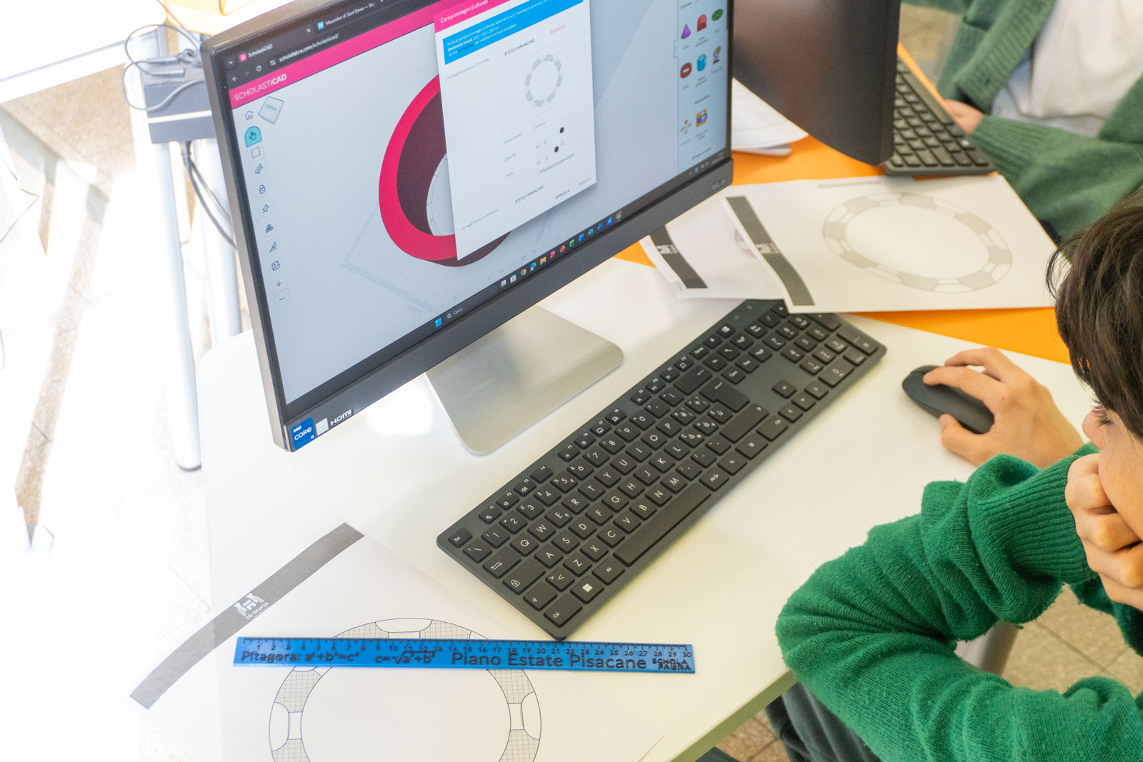 Studente al computer con ScholastiCAD, disegni tecnici su carta e un righello progettato dalla classe